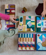 Grimm's wooden panorama building set inside the rectangle frame next to other building sets lying flat on a fluffy carpet