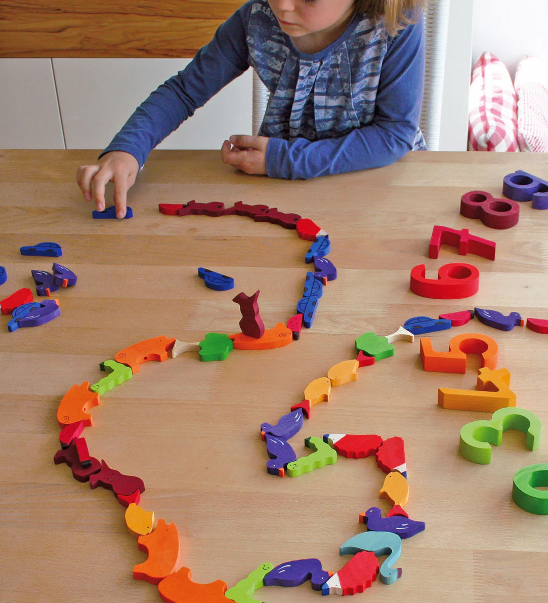 A child playing with the Grimm's Figures For Counting & Story Telling on a wooden table. 