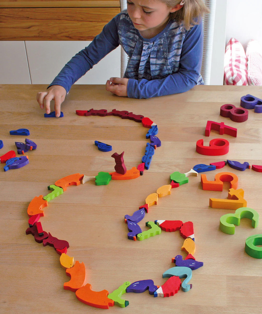 A child playing with the Grimm's Figures For Counting & Story Telling on a wooden table. 