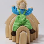 Grimm's Blond Boy Doll - Linde is sat on top of a Grimm's Natural Wooden house with its arms bent up, to show the flexibility of the arms and legs