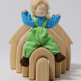 Grimm's Blond Boy Doll - Linde is sat on top of a Grimm's Natural Wooden house with its arms bent up, to show the flexibility of the arms and legs