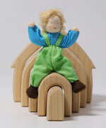 Grimm's Blond Boy Doll - Linde is sat on top of a Grimm's Natural Wooden house with its arms bent up, to show the flexibility of the arms and legs