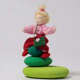 Grimm's Blonde Girl Waldorf Doll sat on top of the Green Grimm's Moss Pebbles Building Set, on a grey background