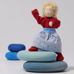 Grimm's Blonde Woman Doll is standing on the Blue Grimm's River Pebble pieces with its legs bent at the knees and its arms stretched up to show the flexibility of the doll
