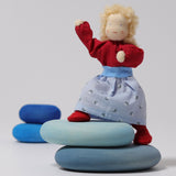 Grimm's Blonde Woman Doll is standing on the Blue Grimm's River Pebble pieces with its legs bent at the knees and its arms stretched up to show the flexibility of the doll