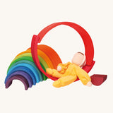 The Grimm's Yellow Soft Doll is relaxing on a Grimm's Wooden Rainbow toy
