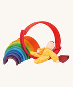 The Grimm's Yellow Soft Doll is relaxing on a Grimm's Wooden Rainbow toy