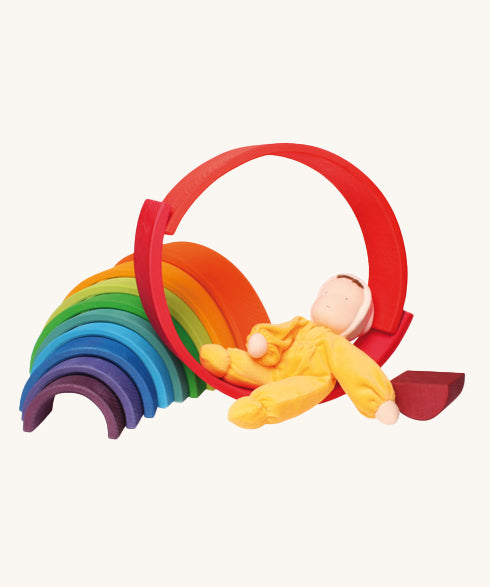 The Grimm's Yellow Soft Doll is relaxing on a Grimm's Wooden Rainbow toy