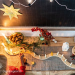 Decorative Christmas table setting with a Grimm's natural spiral celebration ring, candles, a star, and a child's hand holding a candle.