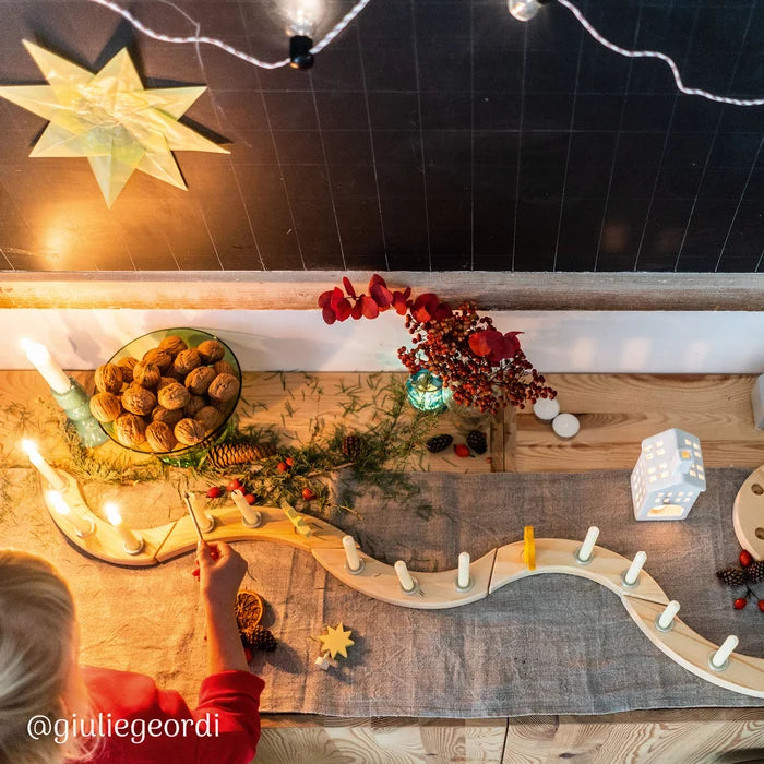 Decorative Christmas table setting with a Grimm's natural spiral celebration ring, candles, a star, and a child's hand holding a candle.