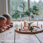 Two children looking at a Grimm's wooden spiral Advent calendar with lit candles on a wooden table.