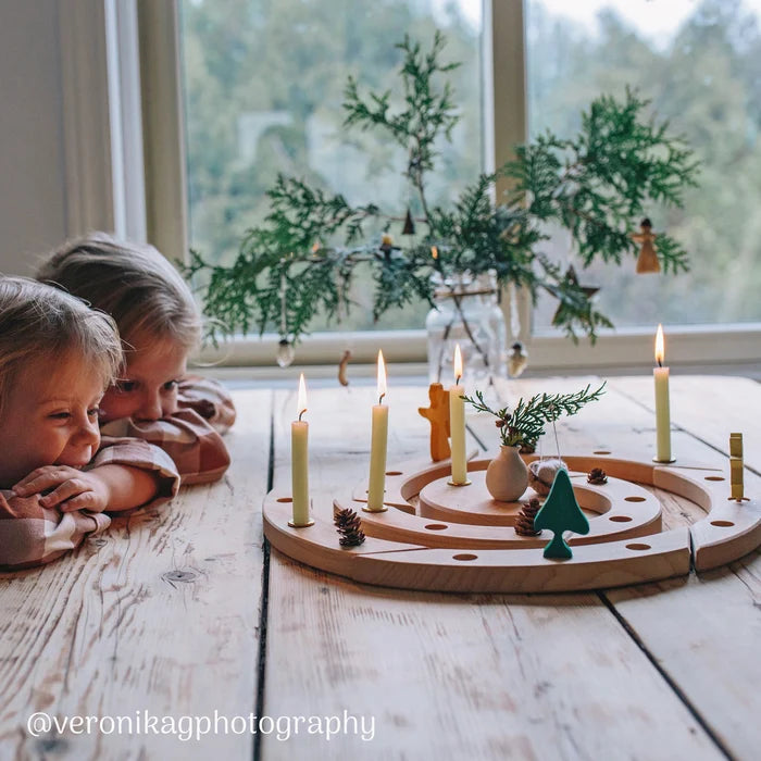 Two children looking at a Grimm's wooden spiral Advent calendar with lit candles on a wooden table.