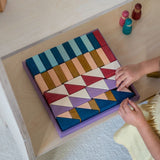 Child arranging different handcrafted wooden Grimms pieces from the rhythm set on a shelf 