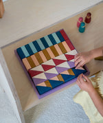 Child arranging different handcrafted wooden Grimms pieces from the rhythm set on a shelf 