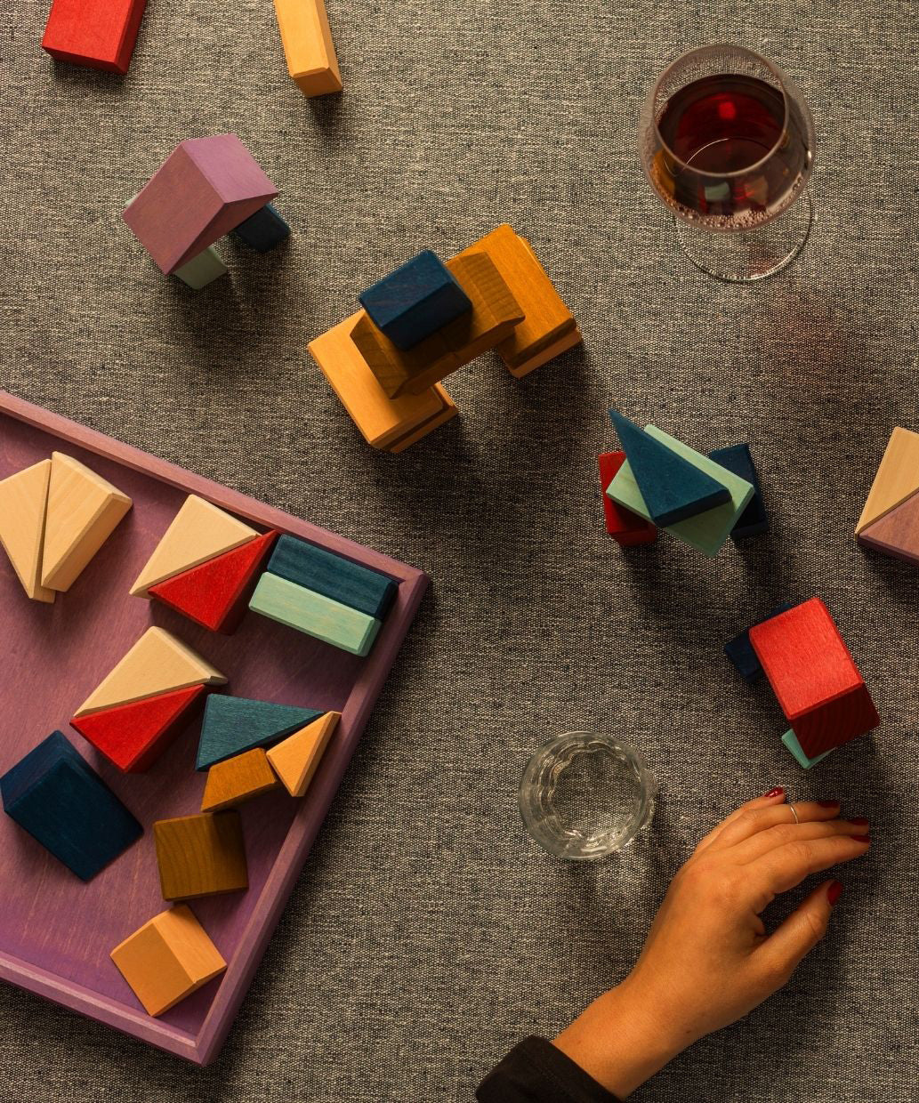 Adult hand stacking different handcrafted wooden Grimms pieces from the rhythm set on a grey cloth