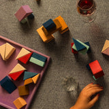 Adult hand stacking different handcrafted wooden Grimms pieces from the rhythm set on a grey cloth