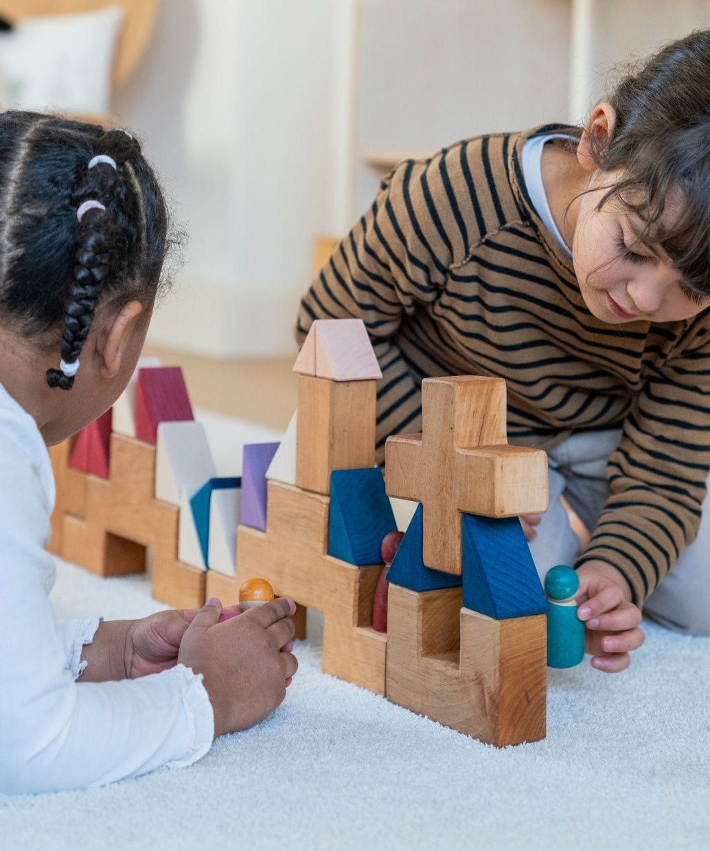 Two children playing with different handcrafted Grimms rhythm pieces on a fluffy rug in a playroom settting