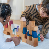 Two children playing with different handcrafted Grimms rhythm pieces on a fluffy rug in a playroom settting