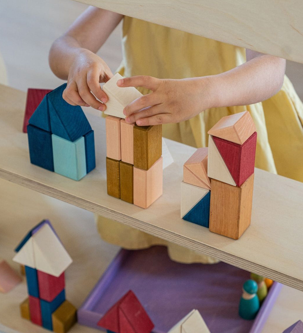 Child stacking different handcrafted wooden Grimms pieces from the rhythm set on a shelf 