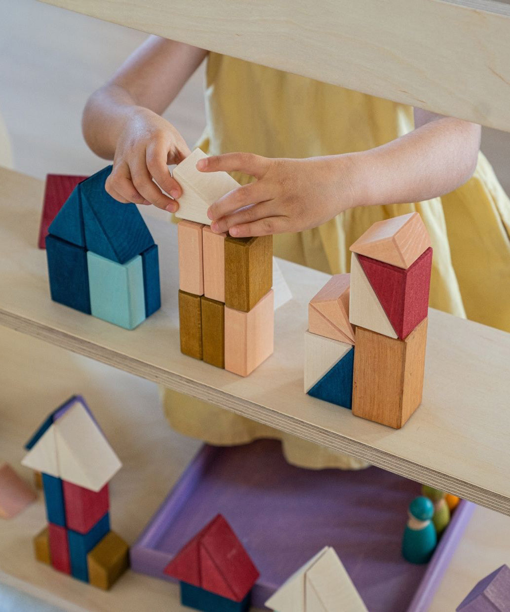 Child stacking different handcrafted wooden Grimms pieces from the rhythm set on a shelf 