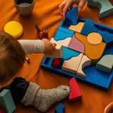 Child holding a Grimm's white handcrafted wooden piece above the blue square frame