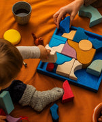 Child holding a Grimm's white handcrafted wooden piece above the blue square frame