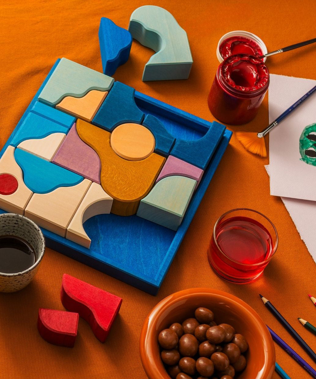 Grimm's wooden wave building set in a blue square frame on a orange cloth next to arts and crafts supplies