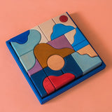 Grimm's wooden wave hand carved pieces in a blue square frame against a light pink background