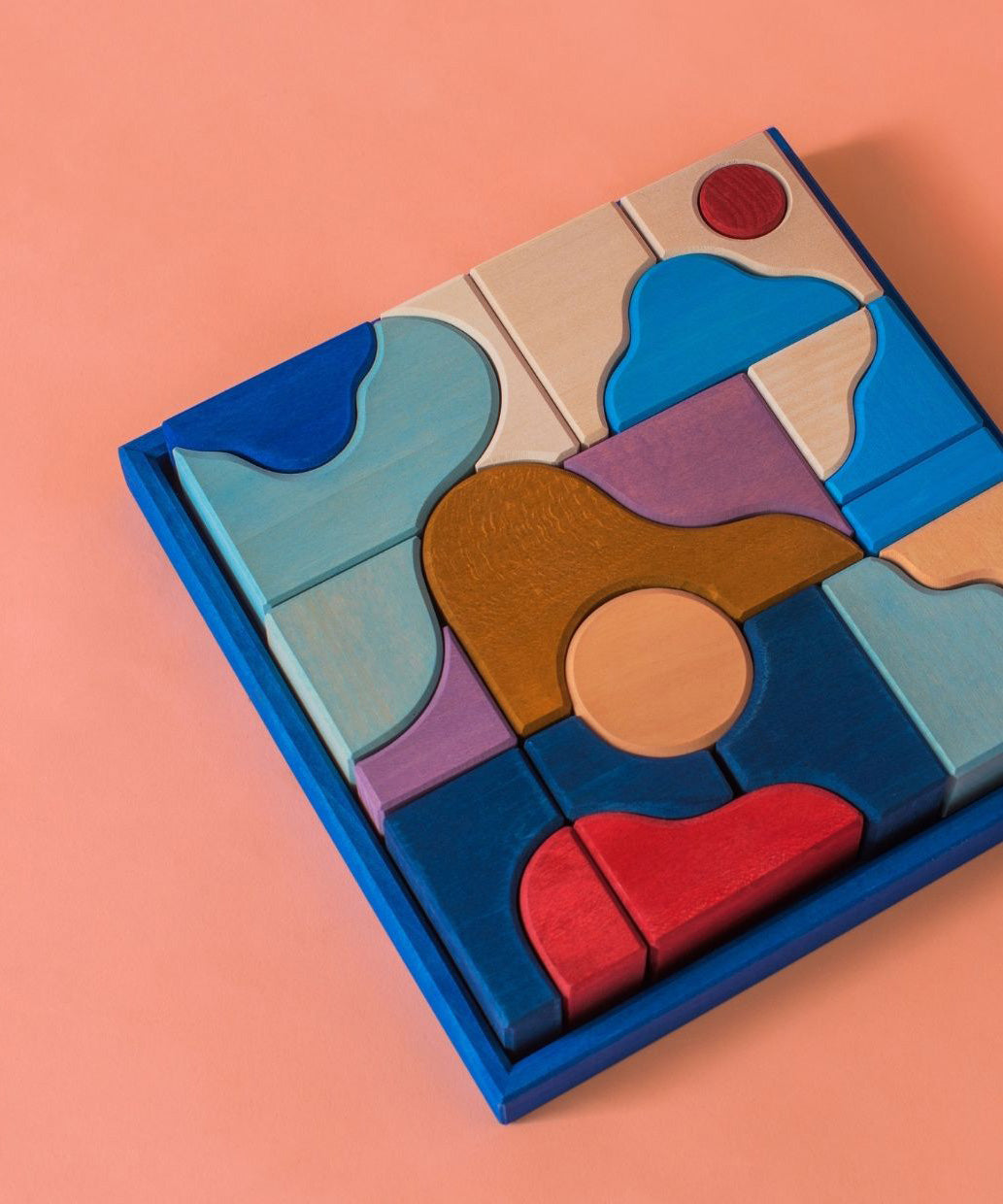 Grimm's wooden wave building set, shows handcrafted piece in a blue frame on a pink background.