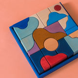 Grimm's wooden wave building set, shows handcrafted piece in a blue frame on a pink background.