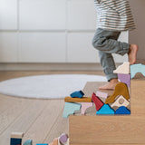 Loose wooden handcrafted piece from the Grimms wave set stacked on stairs with a child in the background.