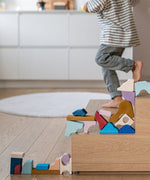 Loose wooden handcrafted piece from the Grimms wave set stacked on stairs with a child in the background.