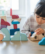 Child stacking hand carved wooden pieces from the Grimms movement set on a table