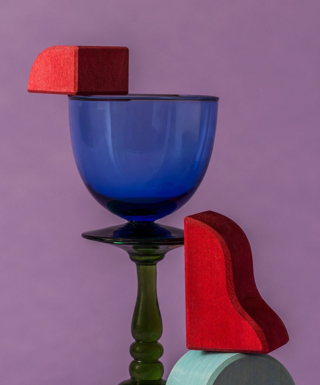 A close up of red handcrafted wooden Grimms pieces from the waves set balancing on a glass