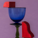 A close up of red handcrafted wooden Grimms pieces from the waves set balancing on a glass