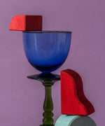 A close up of red handcrafted wooden Grimms pieces from the waves set balancing on a glass