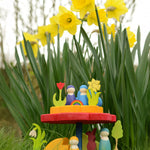 The Grimm's Stacking Flowers Tower, is set down on lush green grass, in front of a patch of daffodils. The stacker has been made into a little display with Grimm's decorative figures and Grimm's friends
