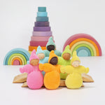 The Grimm's Pastel Dwarfs dolls stood on natural wooden boards, with a selection of Grimm's toys in the background