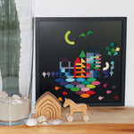 A Grimm's Large magnetic blackboard with a lovely landscape puzzle piece scene. In front of the blackboard is a small Grimm's house and horse. Next to them is a large green cactus in a glass vase