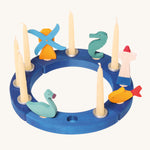 Grimm's 12-Hole Blue Wooden Ring has candles and small Grimm's decorative figures in each hole, and is on a cream background