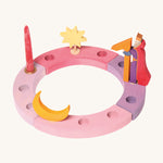 Grimm's 12-Hole Pink-Purple Wooden Celebration Ring with a candle and decorative figures on a cream background