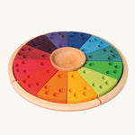 Grimm's Annual Celebration Ring, is made from 12 colourful section with small holes inside ready to lot in candles and colourful numbers, letters and characters into the holes. There is also a small wooden bowl in the middle and it is on a light wooden base. The image is on a cream background