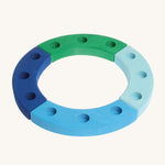 Grimm's 12-Hole Blue-Green Wooden Celebration Ring is made from 4 separate sections of wood with 3 holes to add Grimm's decorative figures and candles inside. The image is on a cream background. 