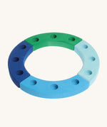 Grimm's 12-Hole Blue-Green Wooden Celebration Ring is made from 4 separate sections of wood with 3 holes to add Grimm's decorative figures and candles inside. The image is on a cream background. 