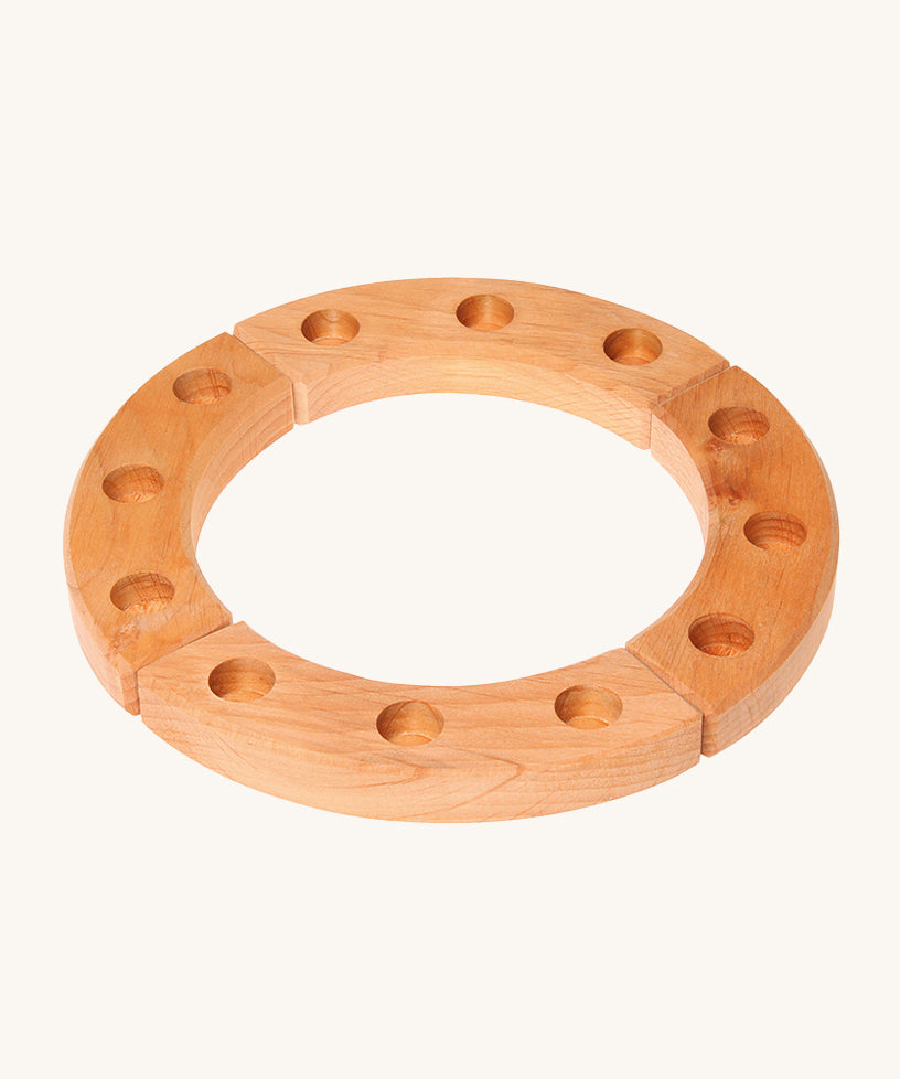 Grimm's 12-Hole Natural Wooden Celebration Ring is made from 4 sections of natural wood with 3 holes in each section, ready for Grimm's decorative figures and candles to be placed inside. The image is on a cream background.