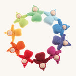 The Grimm's Waldorf Fabric Dwarf Girl dolls are laid in a circle and are each a colour of the rainbow. Each little lady has a fringe and pixie hood and has been crafted by hand. The colour of the dolls are light blue, blue, indigo, pink, magenta, red, orange, yellow, light green and teal on a cream background