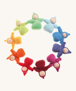 The Grimm's Waldorf Fabric Dwarf Girl dolls are laid in a circle and are each a colour of the rainbow. Each little lady has a fringe and pixie hood and has been crafted by hand. The colour of the dolls are light blue, blue, indigo, pink, magenta, red, orange, yellow, light green and teal on a cream background