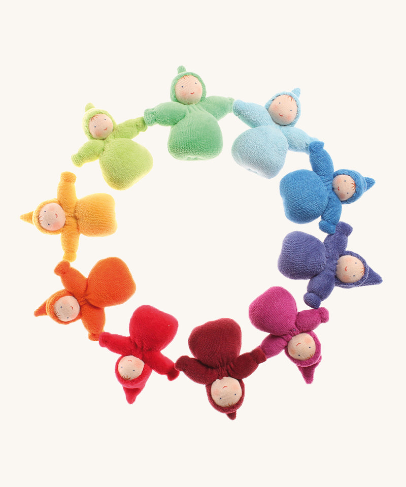 The Grimm's Waldorf Fabric Dwarf Girl dolls are laid in a circle and are each a colour of the rainbow. Each little lady has a fringe and pixie hood and has been crafted by hand. The colour of the dolls are light blue, blue, indigo, pink, magenta, red, orange, yellow, light green and teal on a cream background