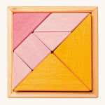 The Grimm's Tangram puzzle toy with blocks in different shapes and sizes, and colours of pink and orange sit in a small light brown wooden base on a cream background