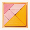 The Grimm's Tangram puzzle toy with blocks in different shapes and sizes, and colours of pink and orange sit in a small light brown wooden base on a cream background